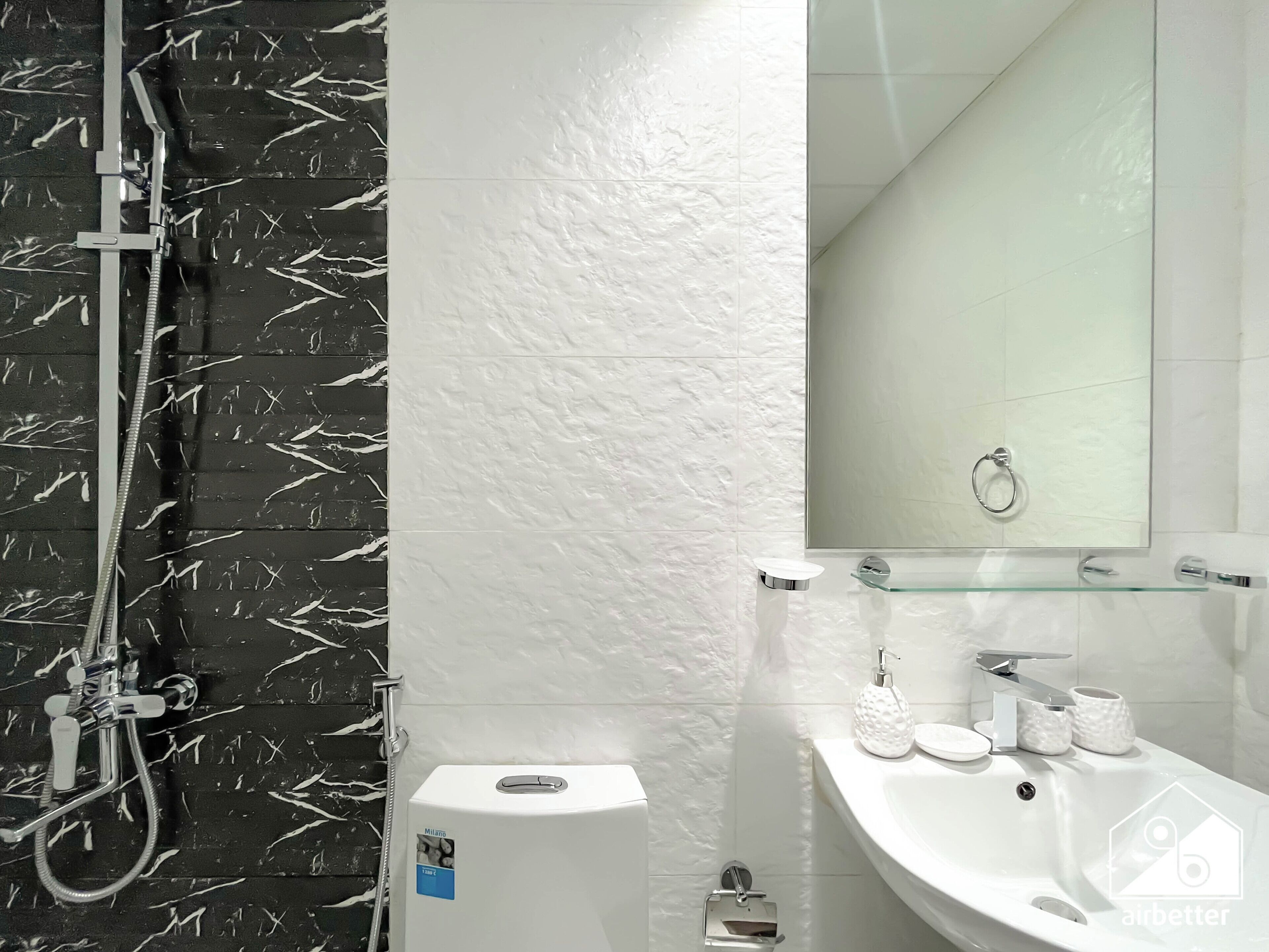 Et moderne badeværelse med en brusevæg i sort og hvid marmor, en væg med struktur, en glashylde med toiletartikler og en hvid vask med et spejl over.