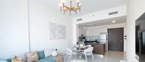 A modern living room with a sofa, coffee table, and dining area. There is a kitchen in the background with white cabinets and a refrigerator.