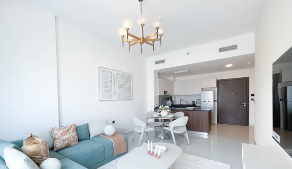 Een moderne woonkamer met een bank, salontafel en een eethoek. In de achtergrond bevindt zich een keuken met witte kasten en een koelkast.