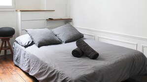 A bedroom with a bed, pillows, a rolled towel, a wooden stool, and a shelf. - Nice studio with Wifi near Montparnasse (Paris)