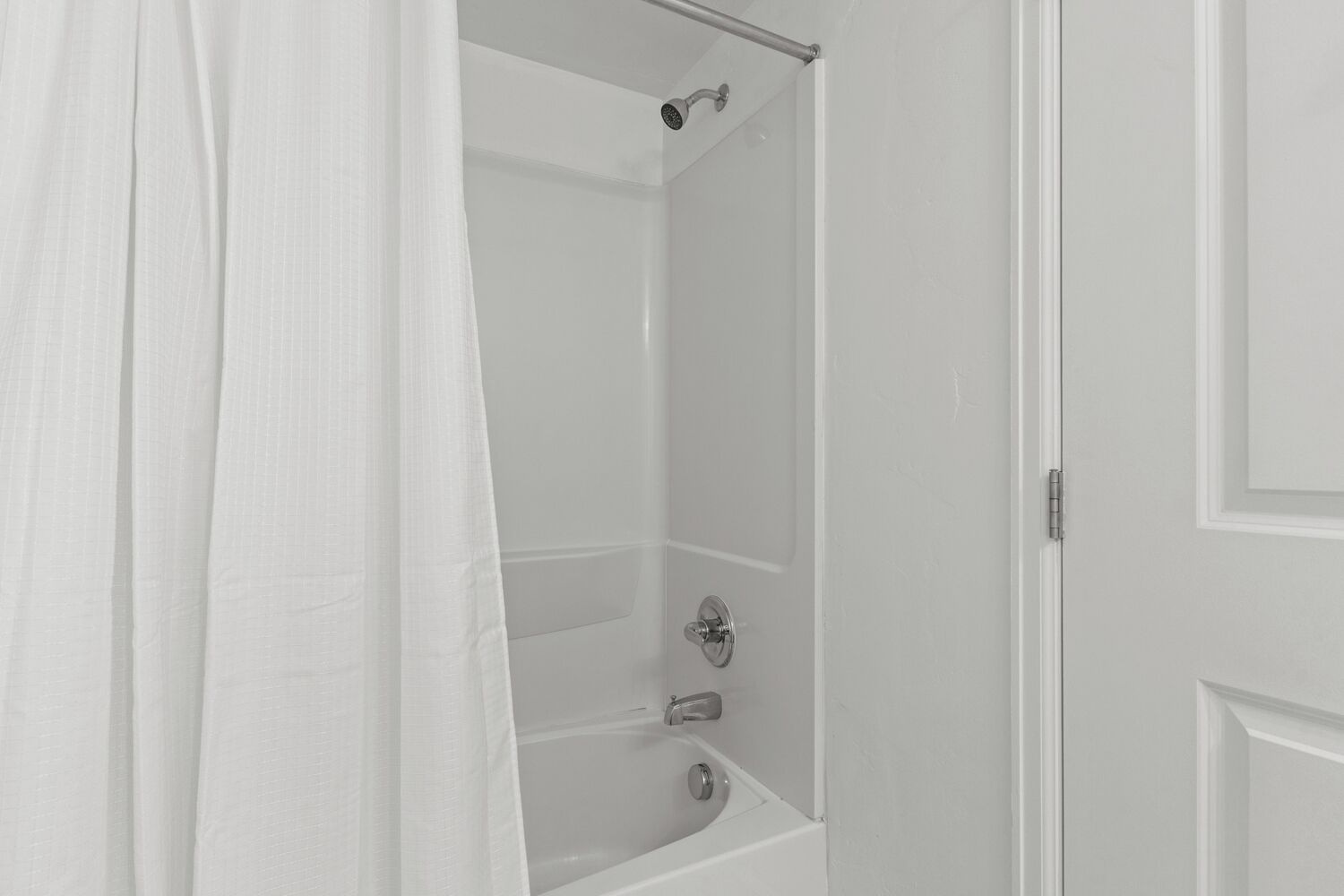 Een badkamer met een douche, bad en een deur.