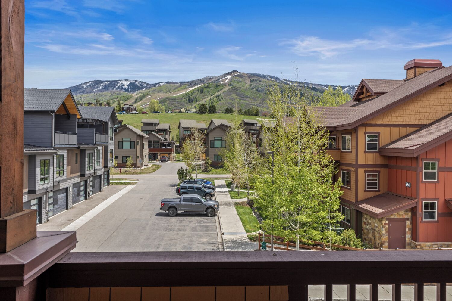 A residential street with houses, parked cars, and a mountain in the background.