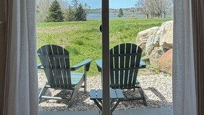A room with a sliding glass door leading to an outdoor seating area with two Adirondack chairs and a table. - Coastal Blue Heron Apartment at Tapley Farm, Blue Hill Peninsula, Acadia (Brooksville)