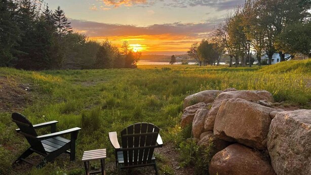 A sunset view with two Adirondack chairs and a small table in a grassy field. - Coastal Blue Heron Apartment at Tapley Farm, Blue Hill Peninsula, Acadia (Brooksville)
