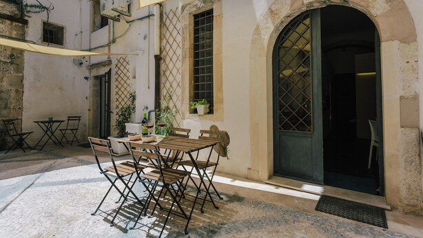 An outdoor patio with a table and chairs, a covered area, and a door with a window. - Studio _ large openspace with kitchen and courtyard (Siracusa)