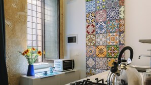 A kitchen with a gas stove, a kettle, a microwave, and a vase with flowers on the counter. - Studio _ large openspace with kitchen and courtyard (Siracusa)