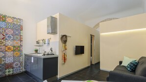 A modern kitchen with a tiled backsplash, a built-in stove, and a dining area with a table and a bowl of fruit. - Studio _ large openspace with kitchen and courtyard (Siracusa)