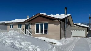 A two-story house with a brown roof and beige siding, surrounded by snow.