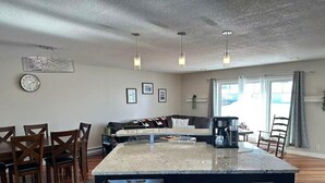 A modern kitchen with a central island, wooden chairs, a coffee maker, and a refrigerator.