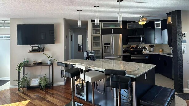 A modern kitchen with a central island, bar stools, stainless steel appliances, and pendant lighting.