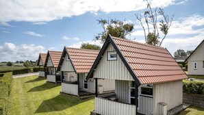 A row of small, single-story cabins with red roofs and white walls, arranged in a grassy area with trees in the background. - 6 Person Holiday Park Home in Faaborg (Faaborg)