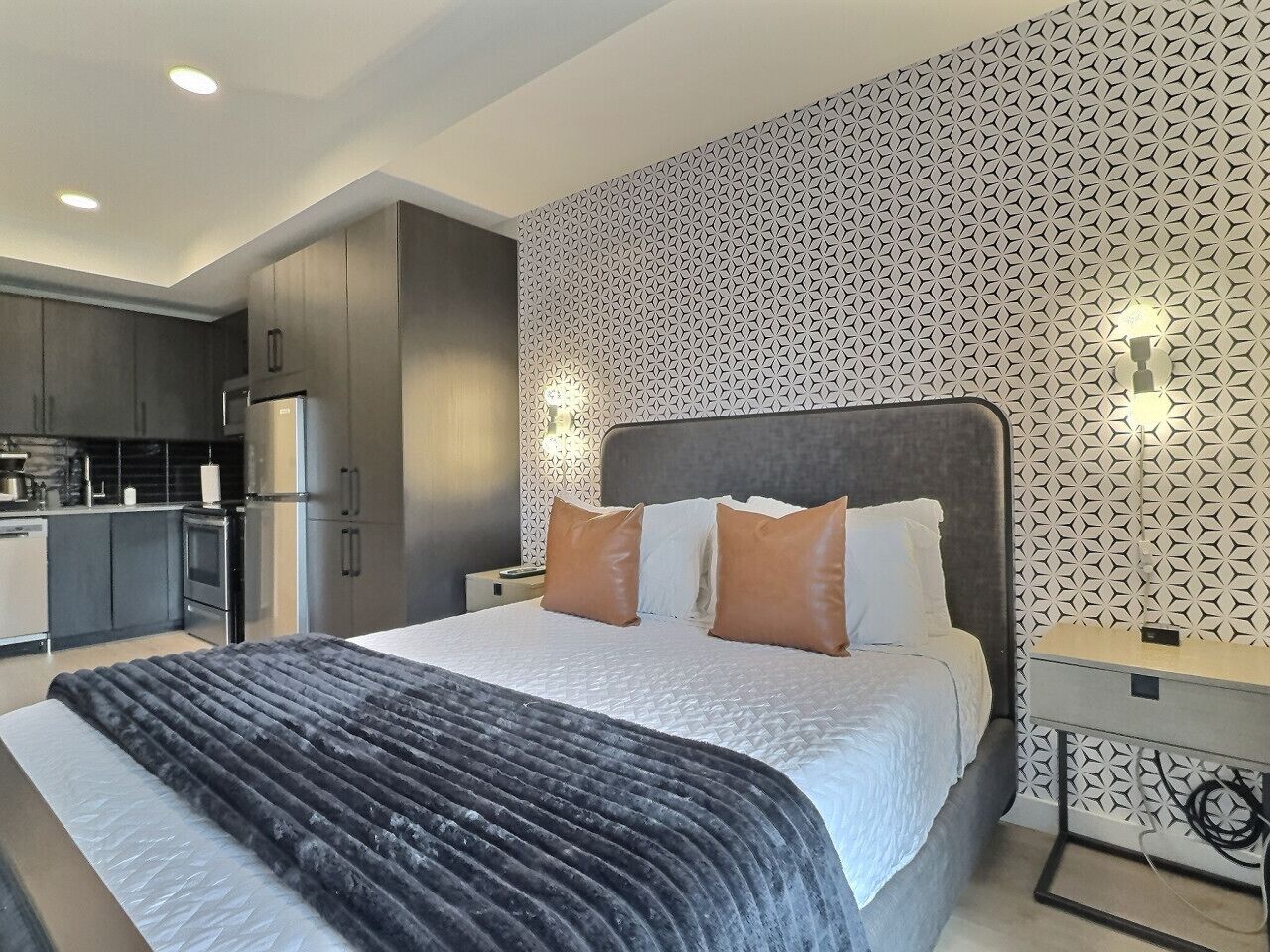 A modern bedroom with a large bed, a headboard, and a nightstand with a lamp.