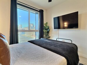 Ein Hotelzimmer mit einem großen Bett, einem flachbildfernseher an der Wand und Blick auf die Stadt durch ein großes Fenster.
