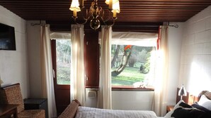 Een slaapkamer met een bed, een stoel, een bureau, een raam met gordijnen en een kroonluchter.
