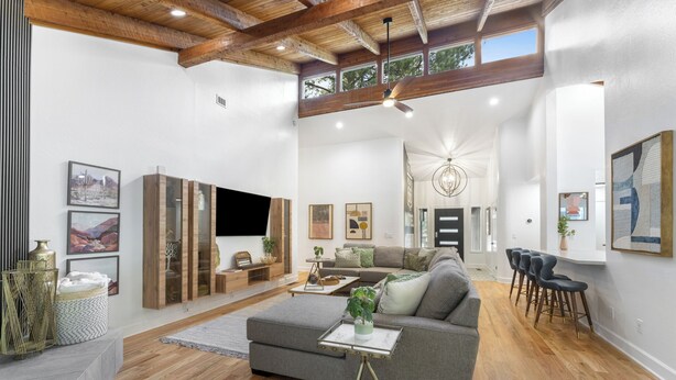 Ein großzügiger Wohnbereich mit grauem Ecksofa, Holzboden und Deckenventilator.