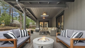 Eine überdachte Terrasse mit zwei grauen Sofas, einer runden Feuerstelle und einem Holztisch.