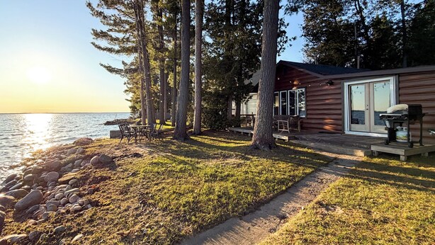 Eine Blockhütte am Seeufer mit einer Terrasse, Sitzgelegenheiten im Freien und Blick auf das Wasser.