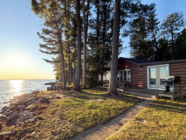 A lakeside cabin with a deck, outdoor seating, and a view of the water.