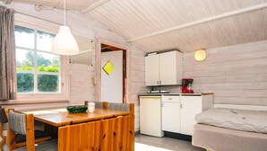 A compact room with a wooden dining table, a single bed, a kitchenette with a red coffee maker, and a window with curtains. - 2 Person Holiday Park Home in Aabenraa (Aabenraa)