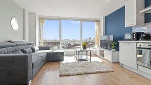 Een moderne woonkamer met een grijze bank, een kleine tafel met een plant en een stadszicht door grote ramen.