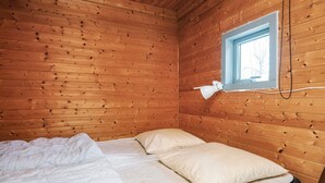 A wooden cabin room with a bed, a window, and a wall-mounted lamp. - 6 Person Holiday Park Home in Pandrup (Pandrup)