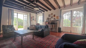 Een gezellige woonkamer met een bank, een salontafel en een boekenkast. Er zijn grote ramen en een deur naar buiten.
