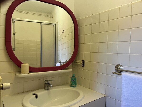 Un baño con un lavamanos blanco, un espejo con marco rojo, un toallero y un dispensador de papel higiénico.