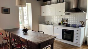 Een keuken met een houten tafel, stoelen, witte kasten, een fornuis en een raam.