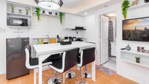 Une cuisine moderne avec un plan de travail blanc, des chaises noires, un réfrigérateur en acier inoxydable et un luminaire suspendu.