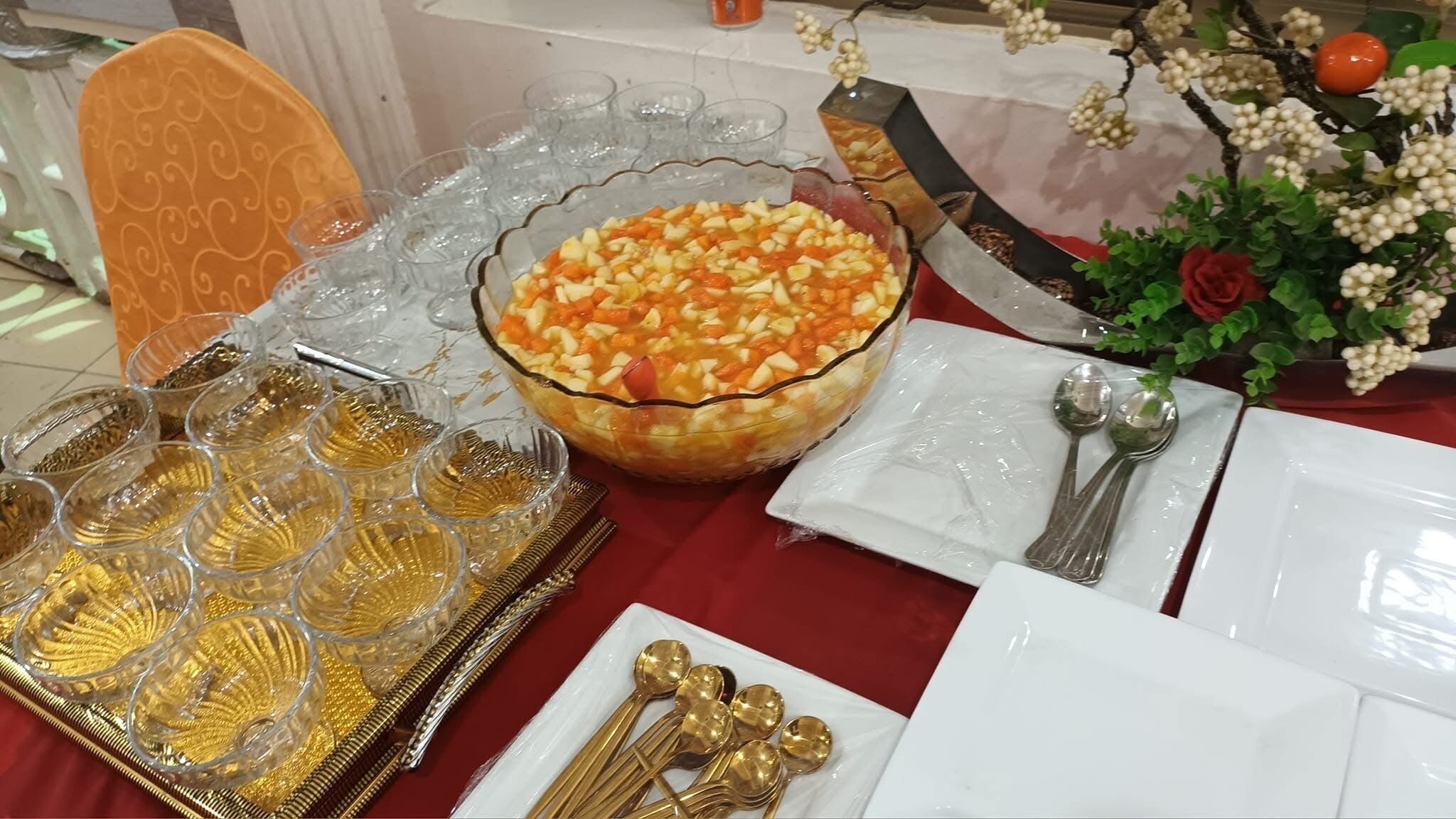 A table set with clear glassware, a bowl of fruit salad, and gold-plated cutlery.