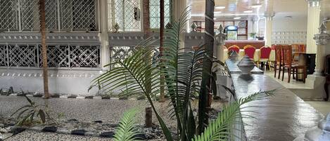 A hotel lobby with a tiled floor, palm trees, a red carpet, and a long table with chairs.