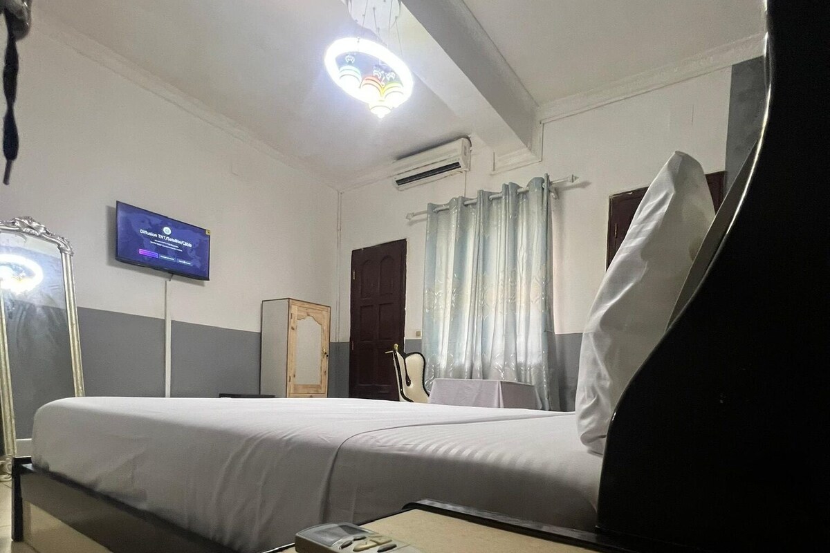Ein Hotelzimmer mit Bett, Wandfernseher, Klimaanlage und einem Vorhangfenster.