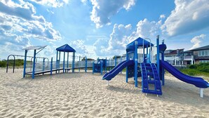 A playground with slides and climbing structures on a sandy beach, surrounded by houses. - Welcome to The Perfect Break — Your Cozy Coastal Getaway! (Lavallette)