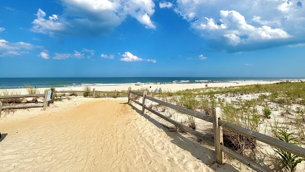 A sandy beach with a wooden fence and sparse vegetation. - Welcome to The Perfect Break — Your Cozy Coastal Getaway! (Lavallette)