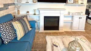 A living room with a blue sofa, a fireplace, and a mounted TV. - Welcome to The Perfect Break — Your Cozy Coastal Getaway! (Lavallette)