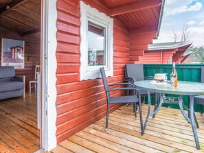 Une terrasse en bois avec une table ronde et des chaises, une bouteille de vin et une affiche accrochée au mur.