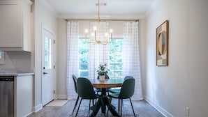 Un comedor con una mesa de madera, cuatro sillas y una araña.
