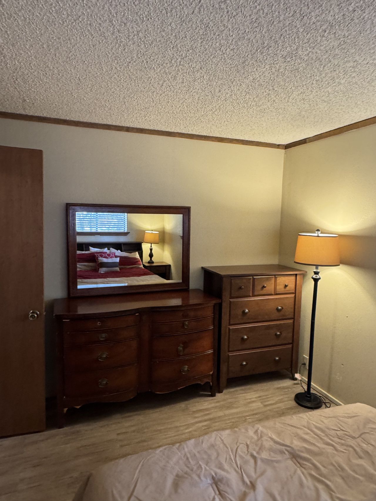 A hotel room with a wooden dresser, a mirror, a lamp, and a bed.