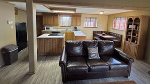 A compact living space with a kitchenette, a leather couch, wooden cabinets, and a dining area. - Beautiful Cabin with Hot Tub (Alto)