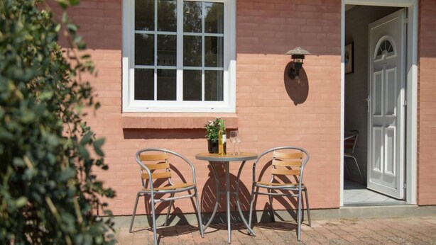 A patio with two metal chairs and a small round table, a window with six panes, and a door to the right. - 2 Person Holiday Park Home in Graested (Graested)
