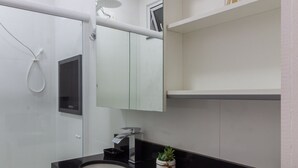 Un baño moderno con encimera negra, armarios blancos, un espejo grande y una pequeña planta en maceta.
