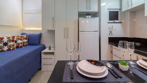 Una cocina moderna con armarios blancos, encimera negra y una mesa de comedor con platos, vasos y cubiertos.