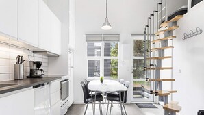 Une cuisine moderne avec des meubles blancs, un coin repas doté d’une table ronde et de chaises, et un escalier avec des marches en bois et des rampes en métal.