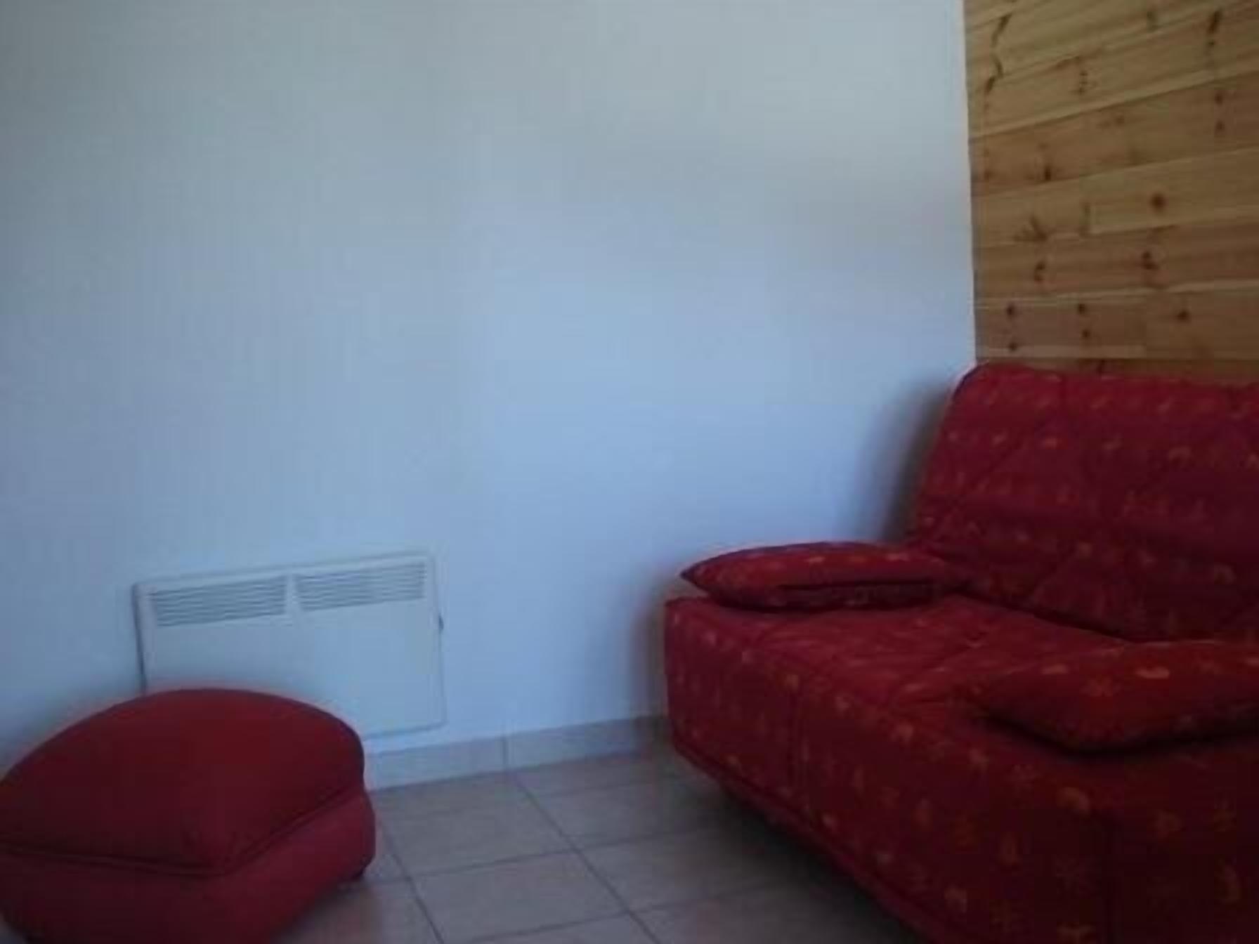A room with a red sofa, a red chair, and a white radiator on the wall.