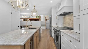 A modern kitchen with a marble countertop, stainless steel appliances, and a wooden floor. - Renovated Retreat with Heated Pool (Redding)