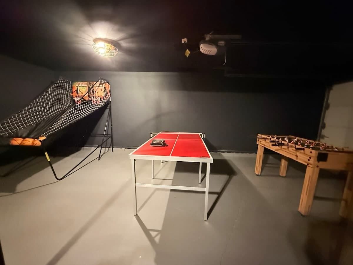 A room with a ping pong table, a foosball table, and a netted area.