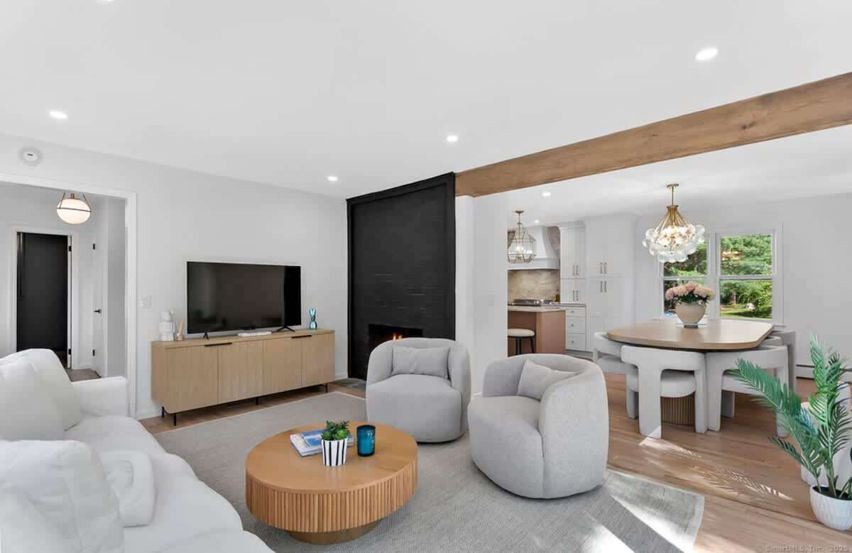 Een moderne woonkamer met een flatscreen televisie, een open haard, een eethoek met tafel en stoelen, en een keuken op de achtergrond.
