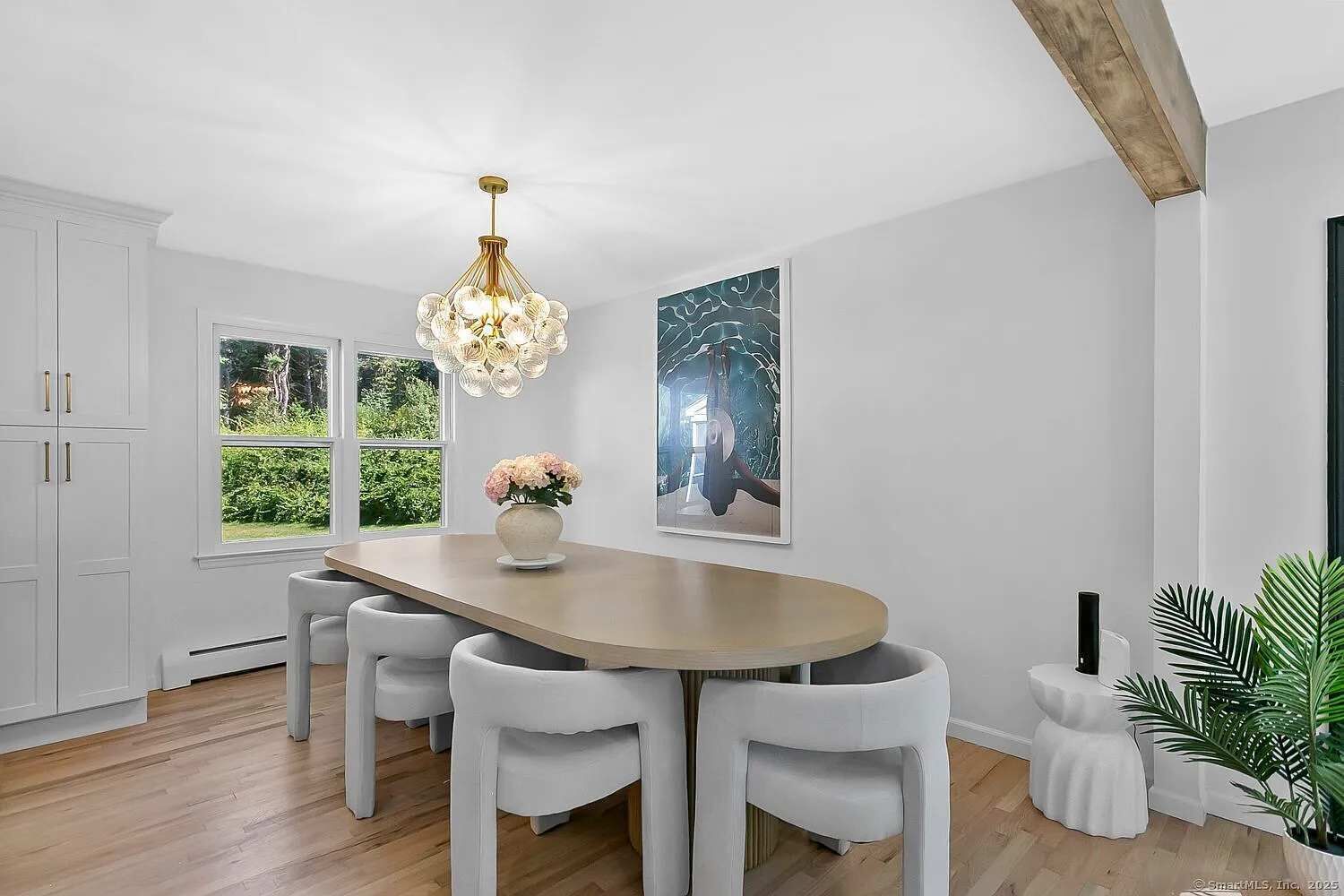 A dining area with a wooden table, white chairs, a chandelier, and artwork on the walls.