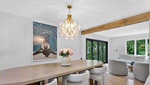 A modern dining area with a wooden table, white chairs, a chandelier, and a painting on the wall. - Renovated Retreat with Heated Pool (Redding)