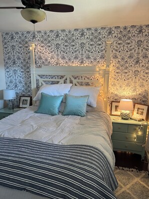 Une chambre avec un lit blanc, des coussins turquoise et un papier peint à motifs.
